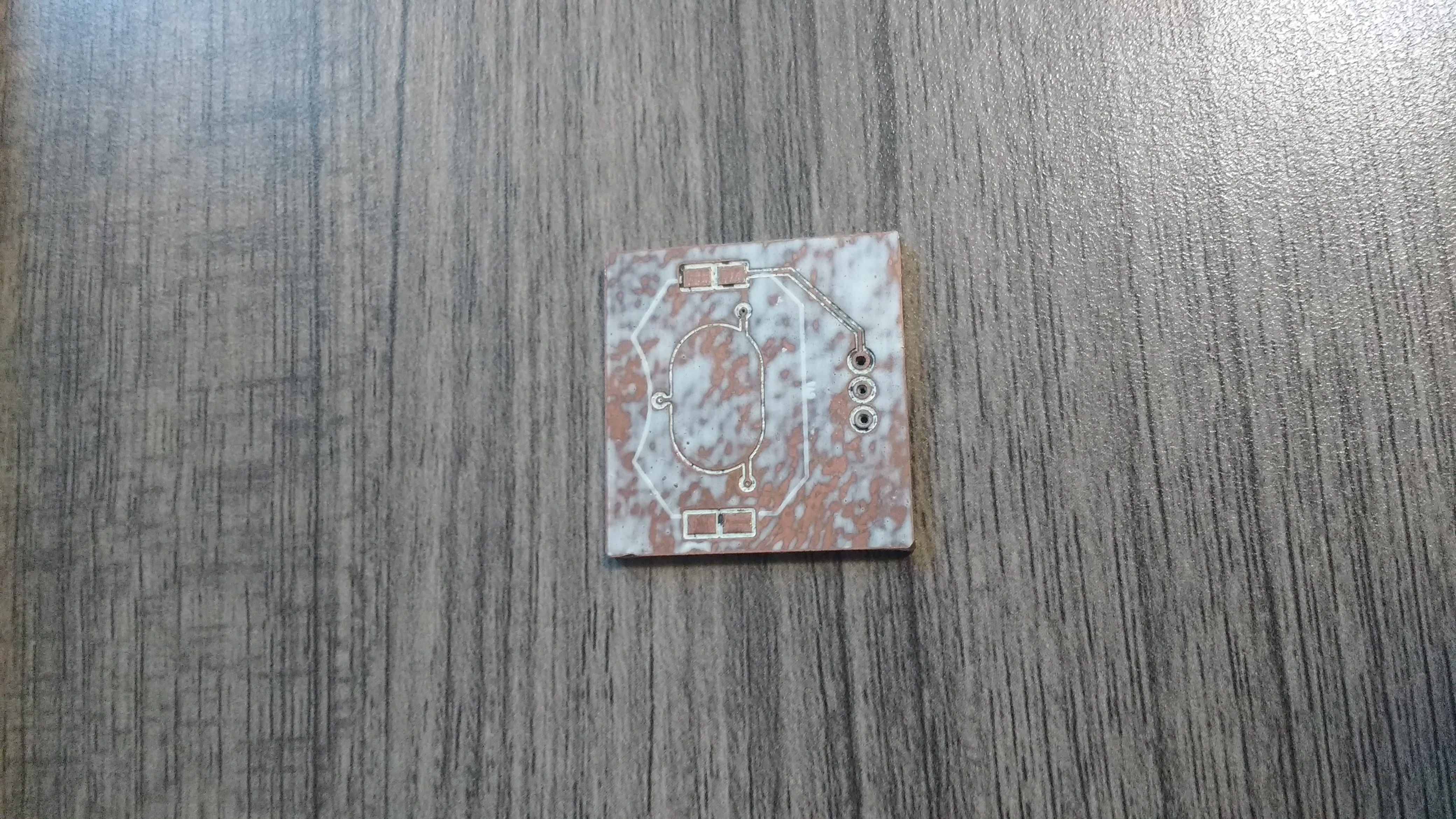 the bottom a 1 inch by 1 inch  copper PCB, with white paint covering its surface.  It has pads for a battery holder