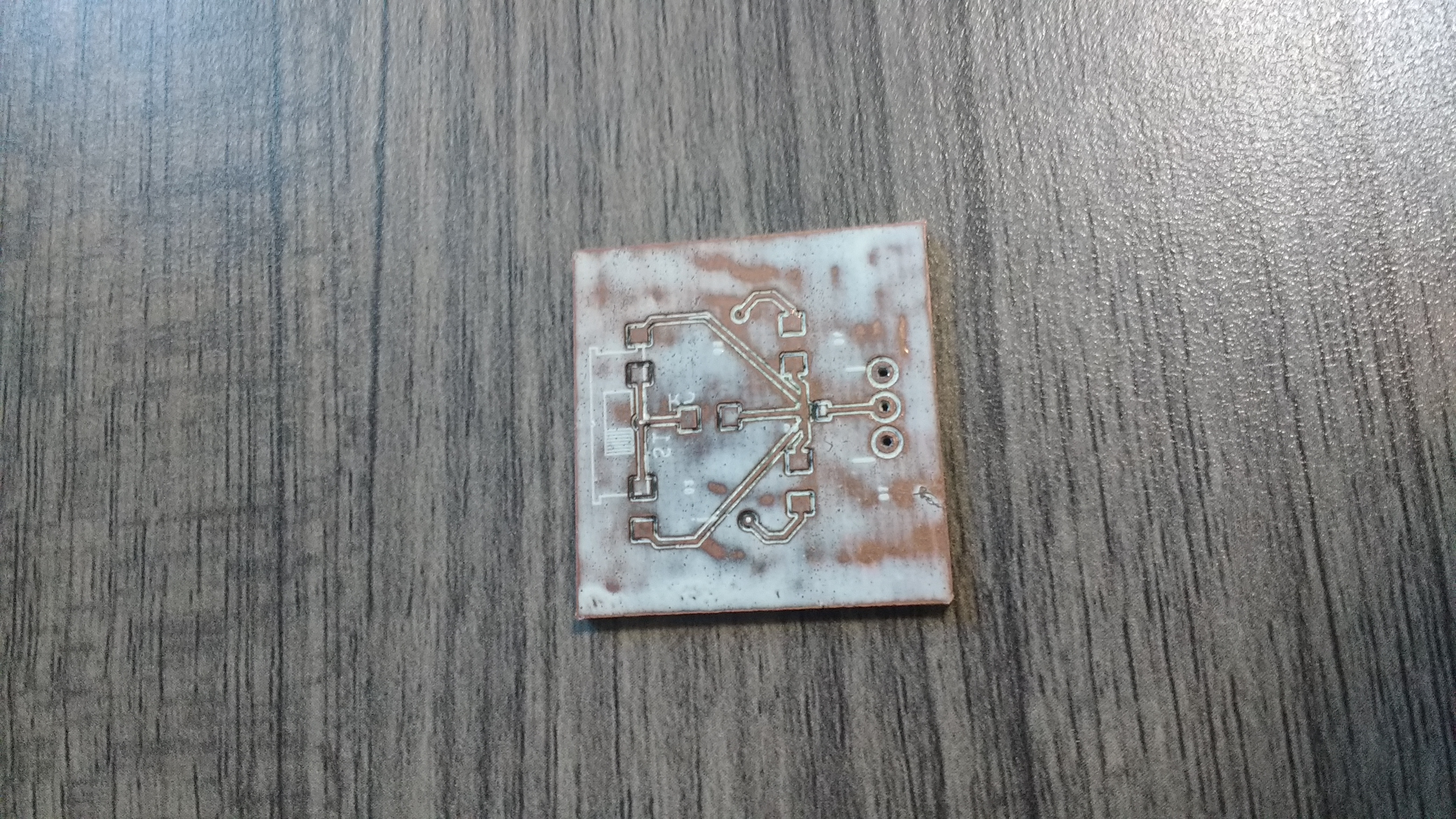 the top of a 1 inch by 1 inch copper PCB, with white paint covering its surface.  It has pads for resistors and leds