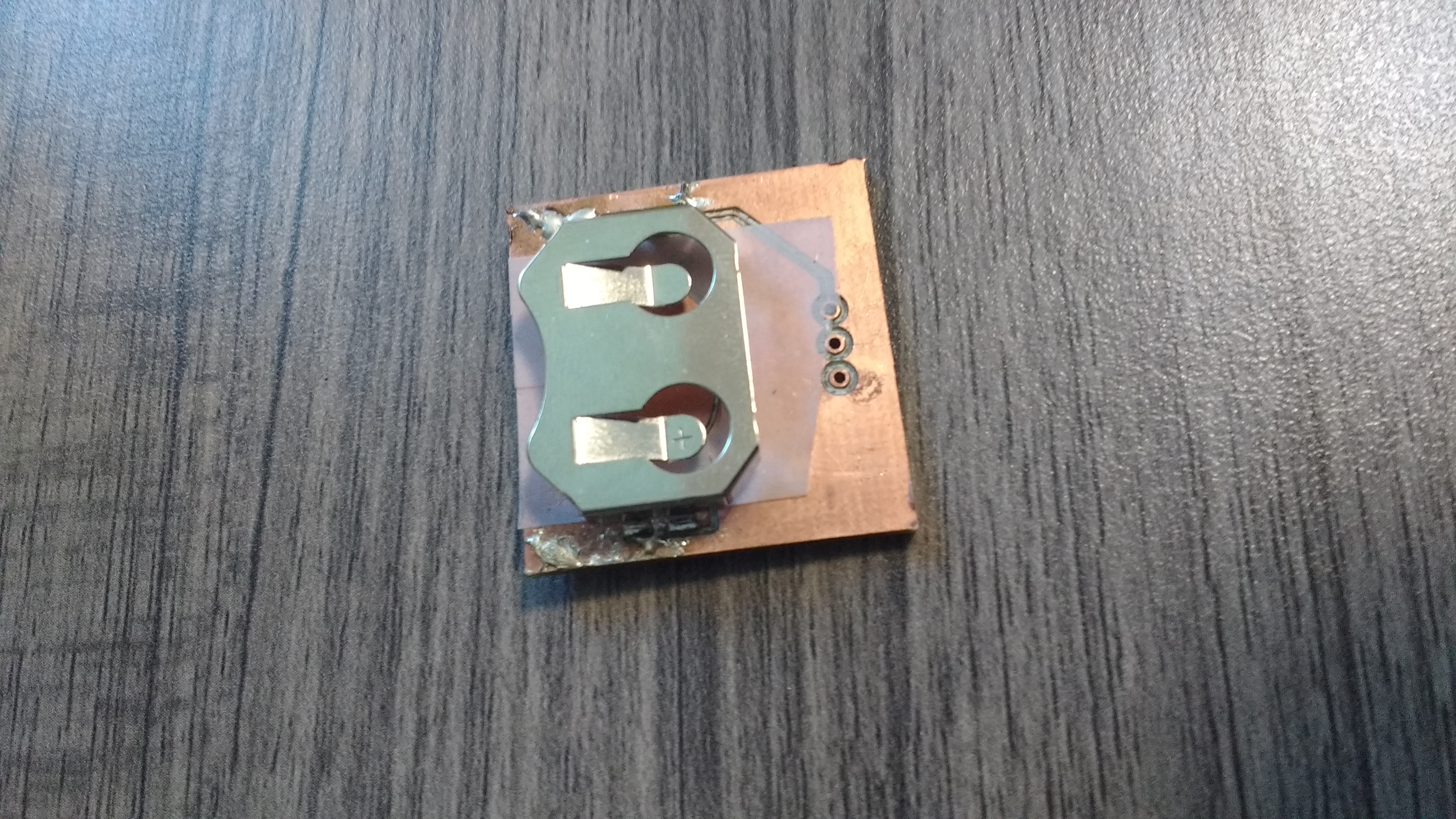 the bottom a 1 inch by 1 inch  copper PCB.  It has a battery holder soldered onto it