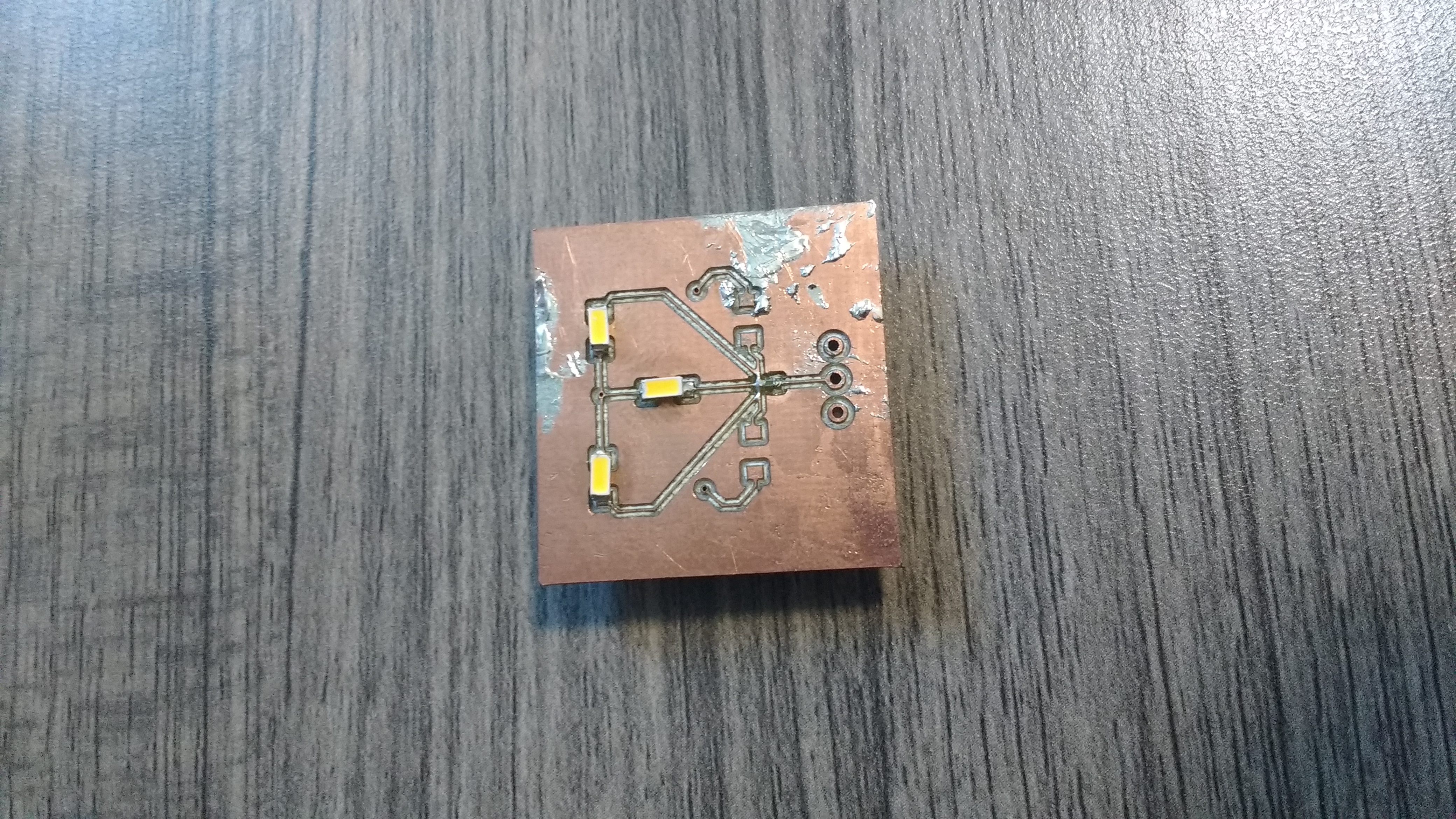 the top of a 1 inch by 1 inch copper PCB. It has resistors and leds soldered onto it