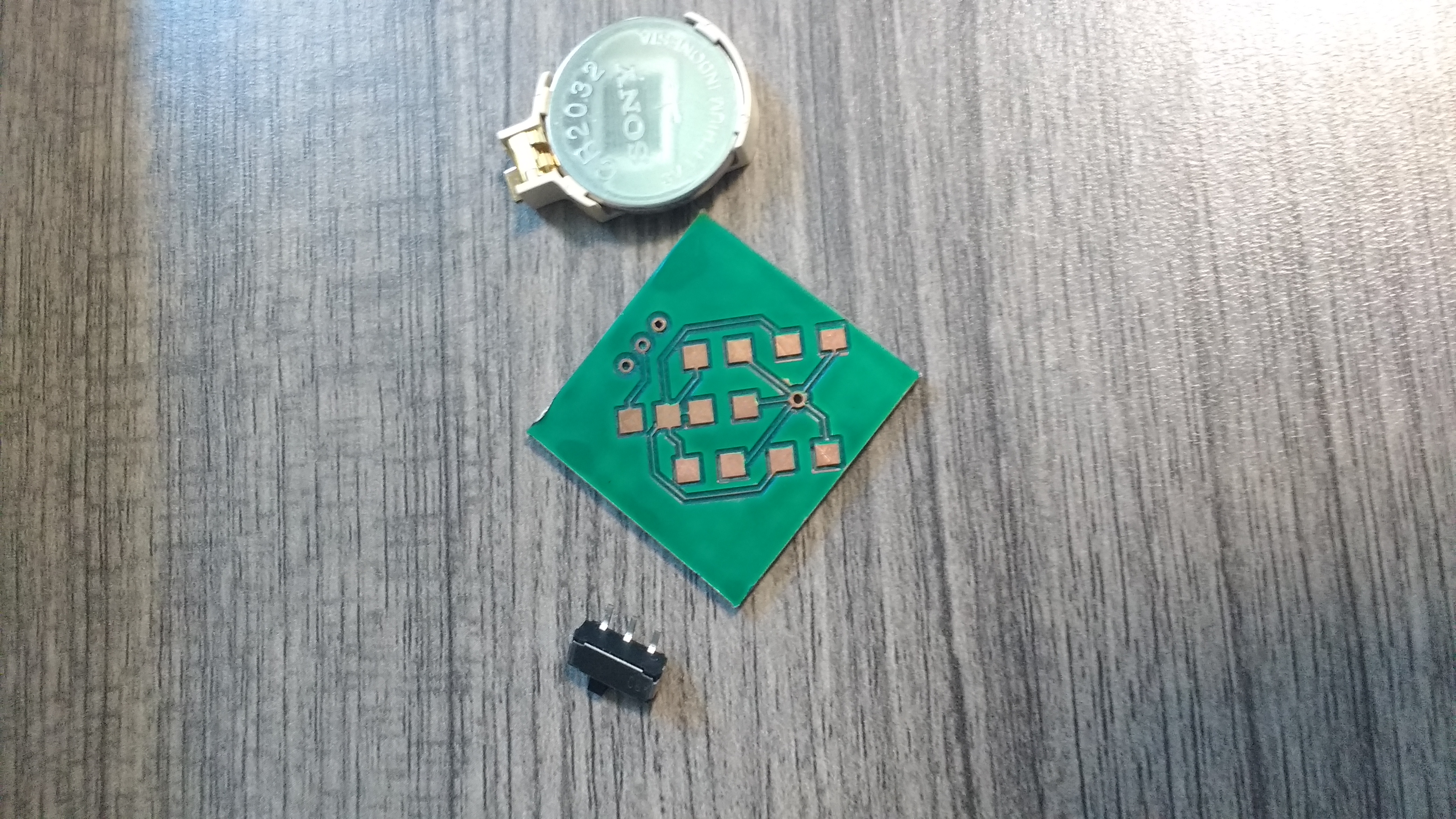 the top of a 1 inch by 1 inch copper PCB. It has green insulation on it, with large exposed copper pads for soldering leds and resistors.